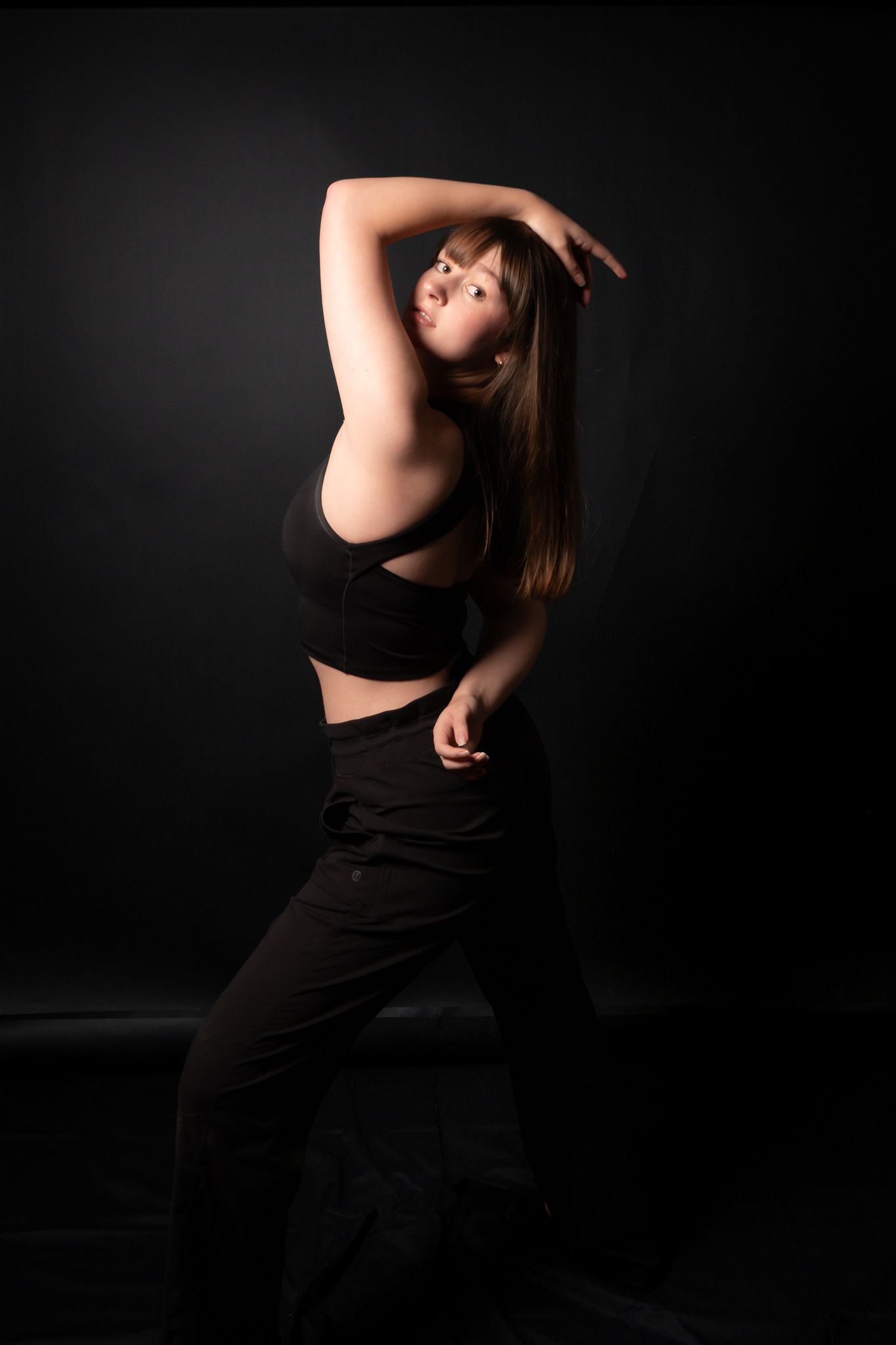 Dancer in black outfit strikes graceful pose against dark background.