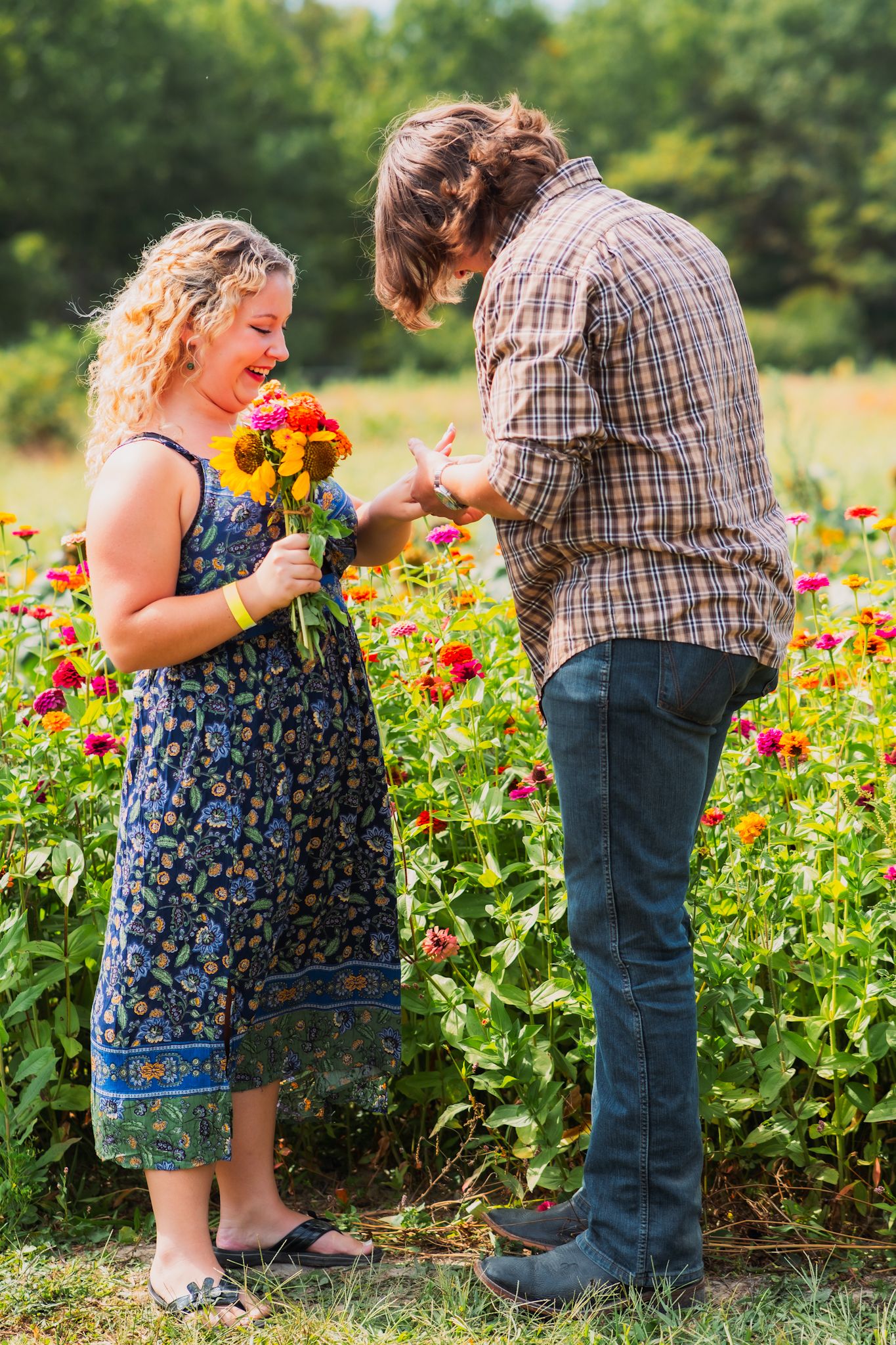 Two people share a tender moment surrounded by vibrant zinnias and sunflowers in a garden setting.