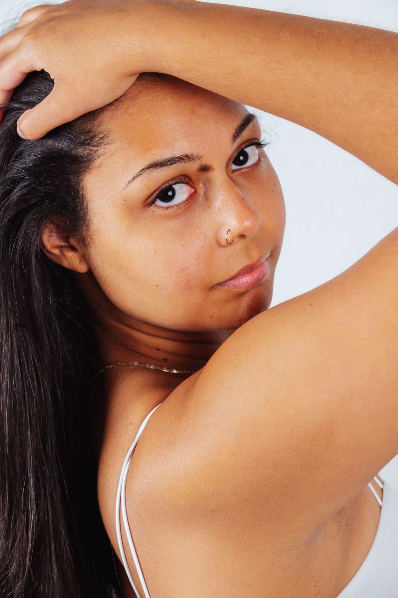 Close-up portrait with natural lighting showcasing silver necklace and white top.