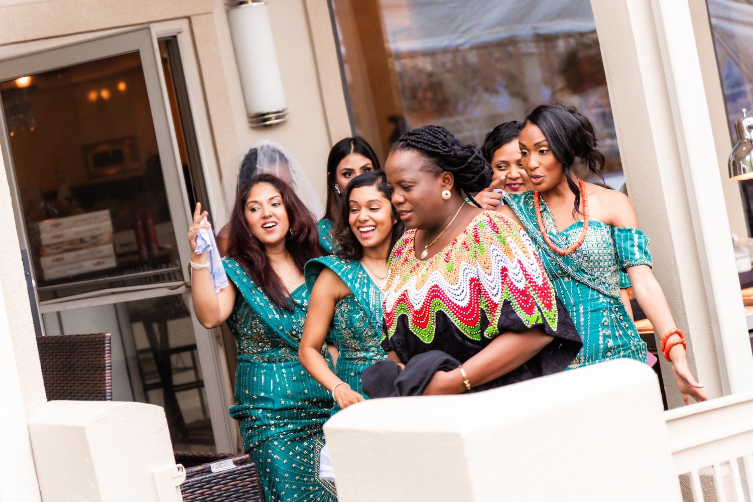 Wedding party members in teal dresses pose together on a porch.