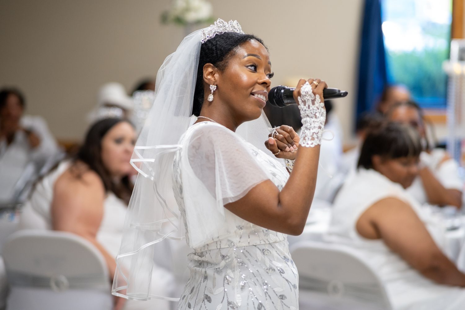 A bride in a white lace dress and veil smiling during her wedding reception.