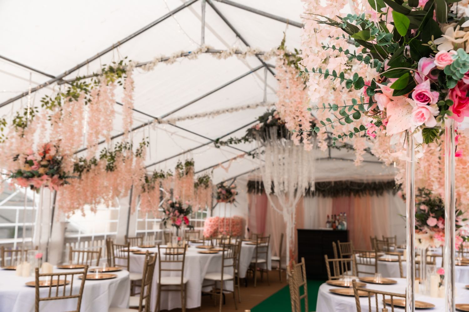 Wedding reception tent decorated with pink floral arrangements and hanging crystal chandeliers.