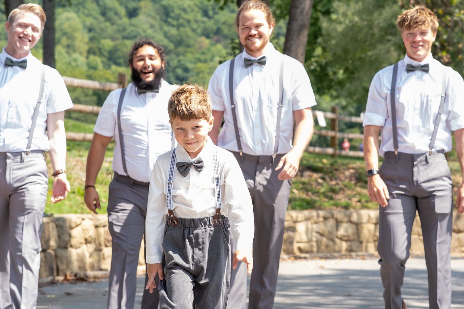 Wedding party members in matching grey pants and suspenders walking together outdoors.