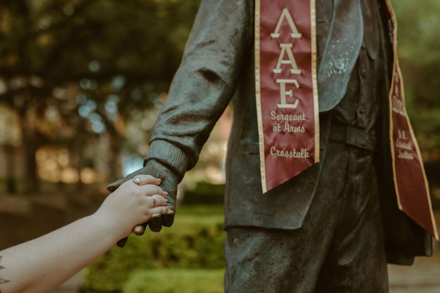 Detail shot of a Texas State University graduate holding the hand of the historic LBJ statue on campus in San Marcos, Texas.