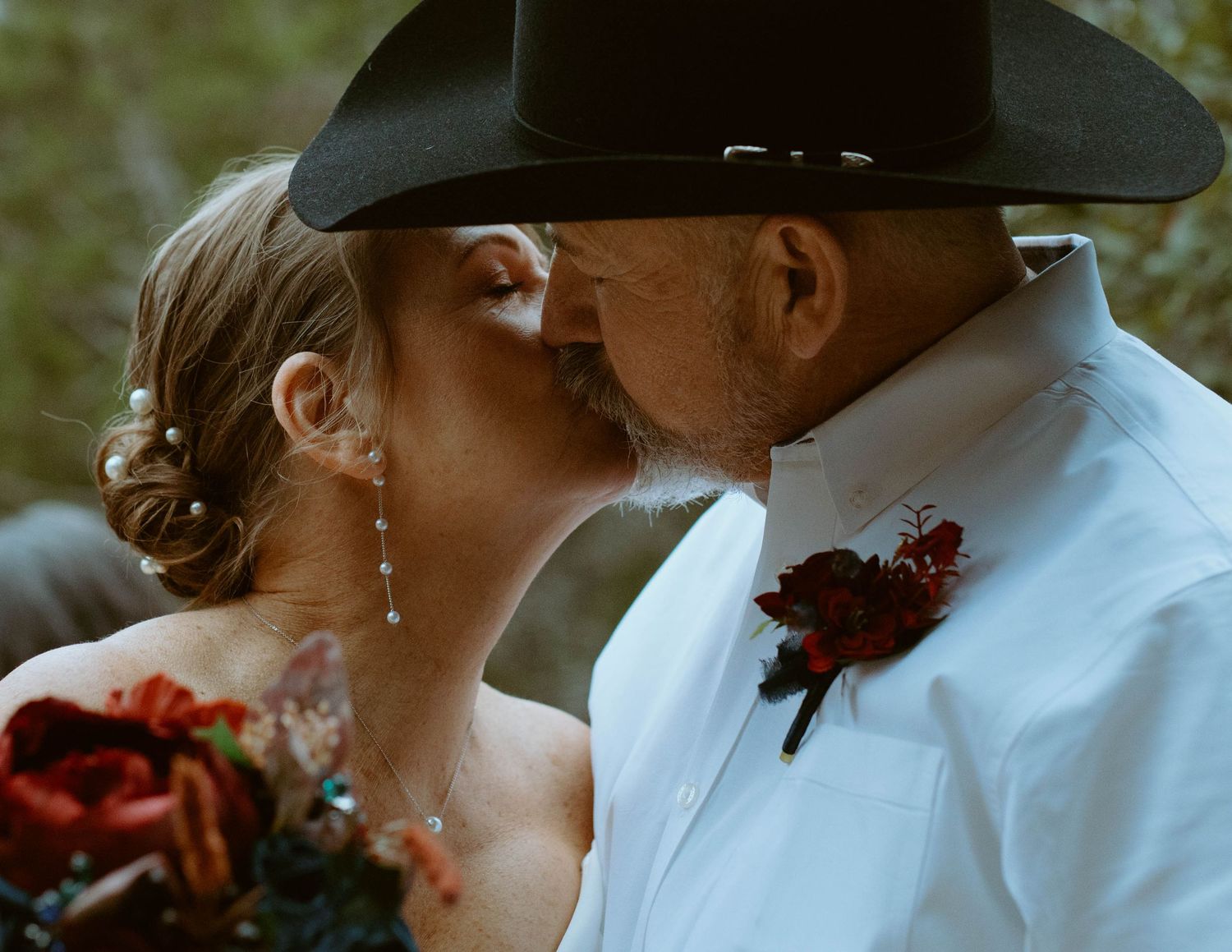 Close-up wedding portrait of a bride kissing her groom, who is wearing a black cowboy hat, during an outdoor Wimberley, Texas wedding.