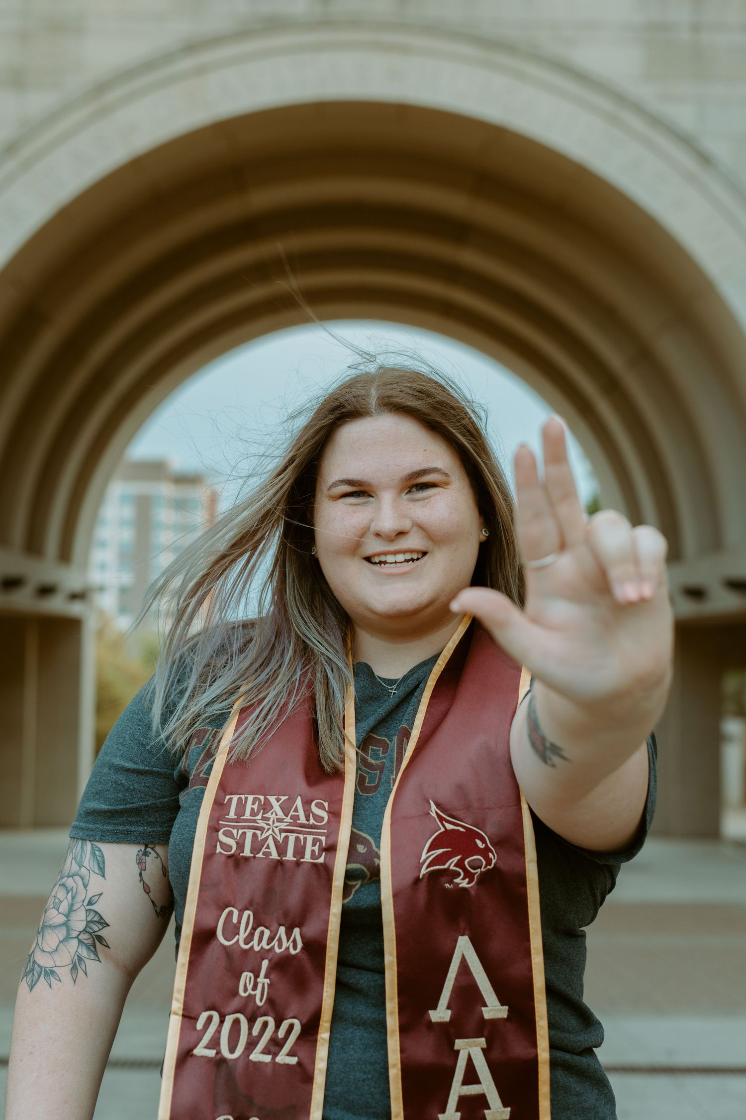TXST senior portrait of a smiling graduate wearing a maroon Class of 2022 stole under a stone archway in San Marcos, Texas.