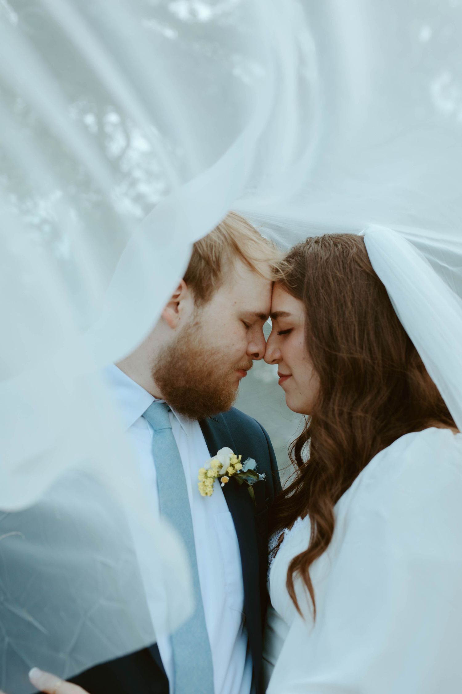 Intimate wedding portrait of a bride and groom touching foreheads while framed softly beneath a flowing white veil at a Wimberley, TX photos