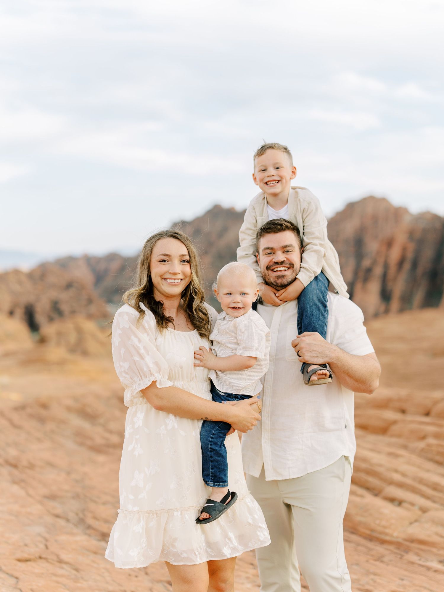 A family poses together in white outfits against a backdrop of red rock formations in the desert.