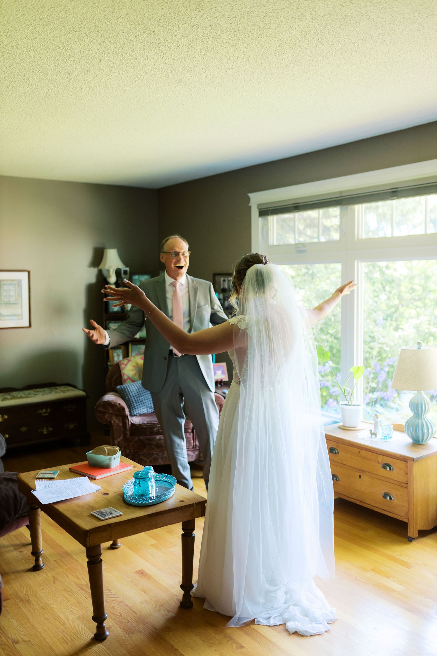 Father reacts with joy seeing bride in wedding dress and veil during emotional first look moment indoors.