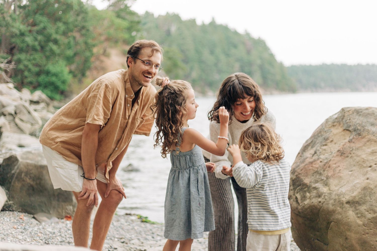 Family sharing playful moments together on a rocky beach with water in the background.