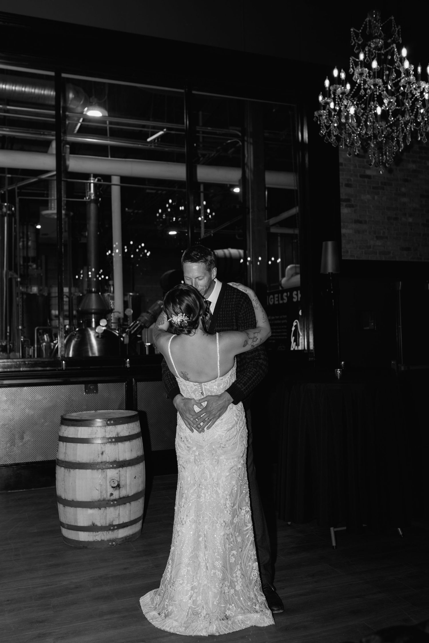 Black and white photo of a bride and groom sharing their first dance at a wedding reception with a chandelier.