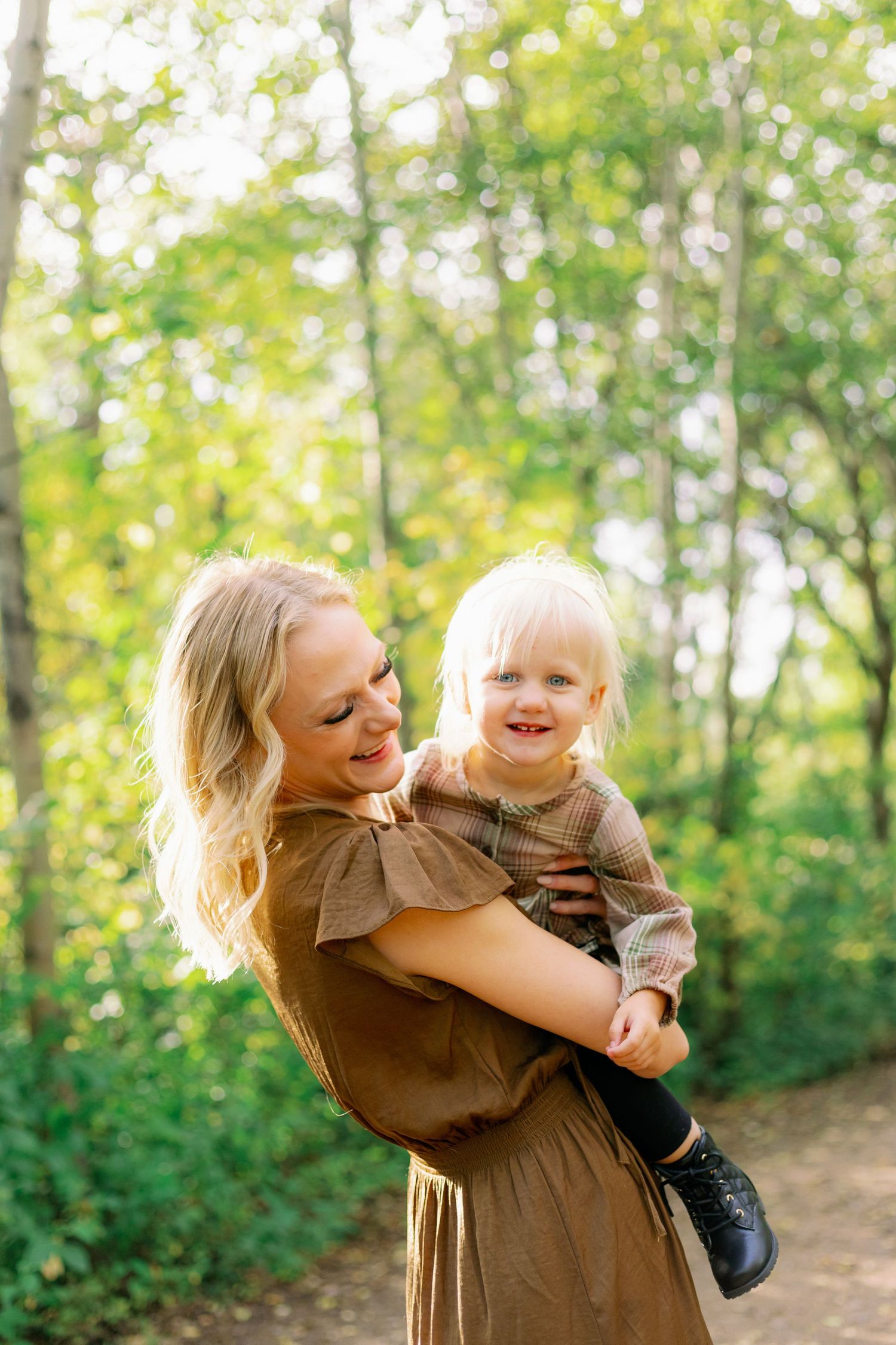 Mother and child share joyful moment together in sunlit forest setting.