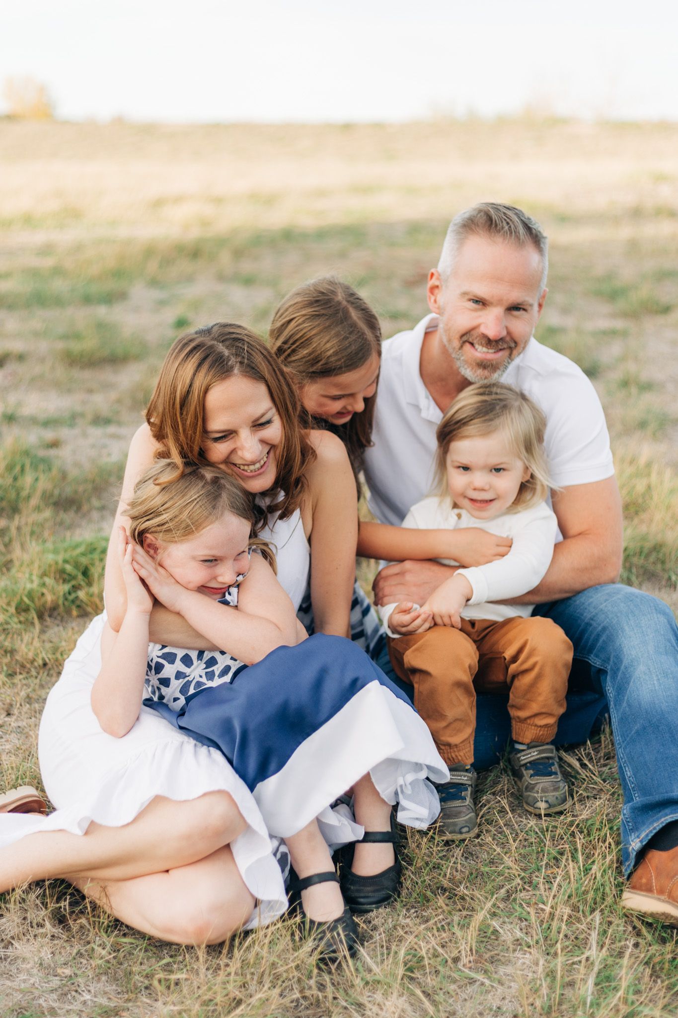 Candid family portrait showing joyful laughter while sitting together in golden field.