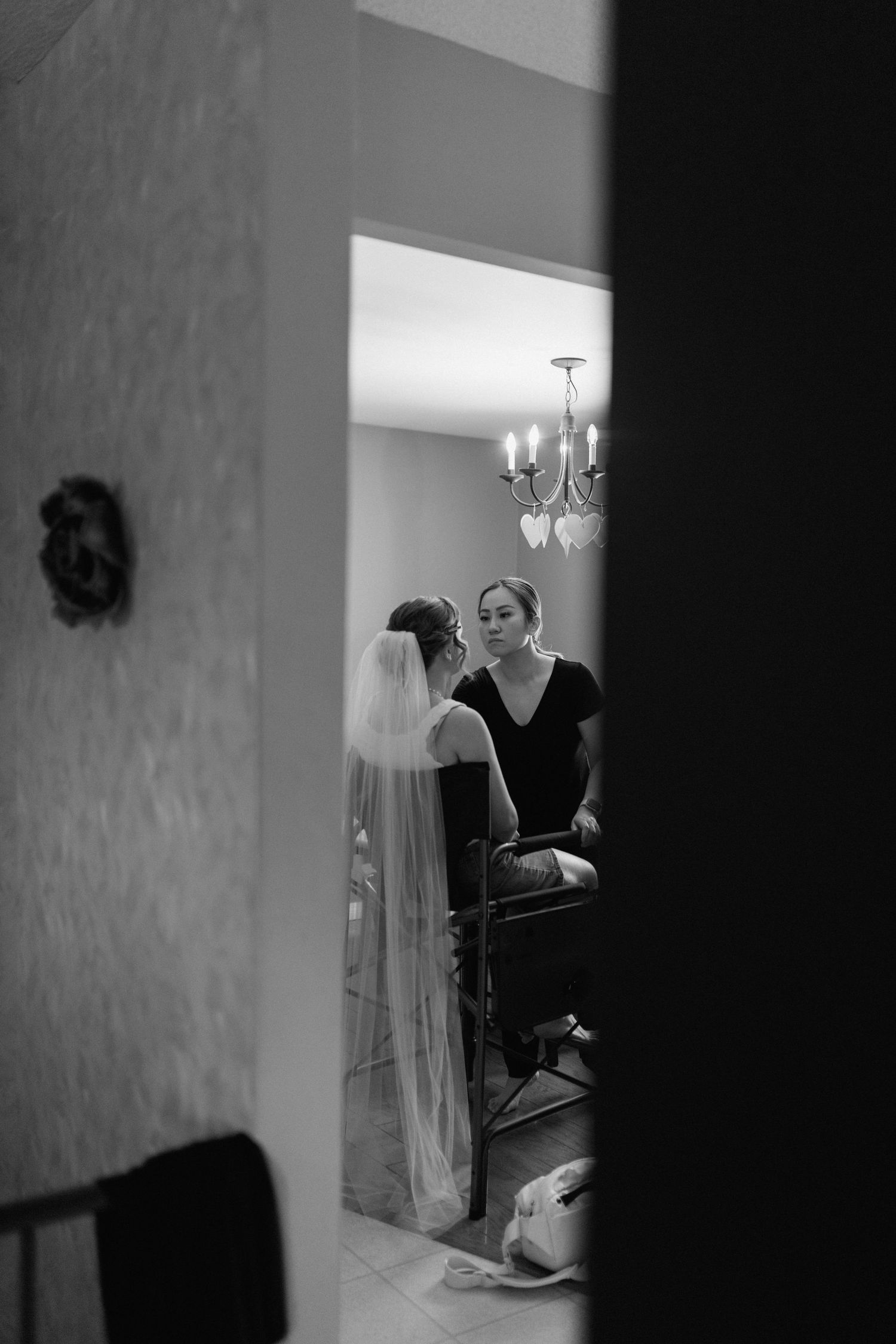 Black and white photo of a bride having her makeup done while wearing a veil before her wedding ceremony.