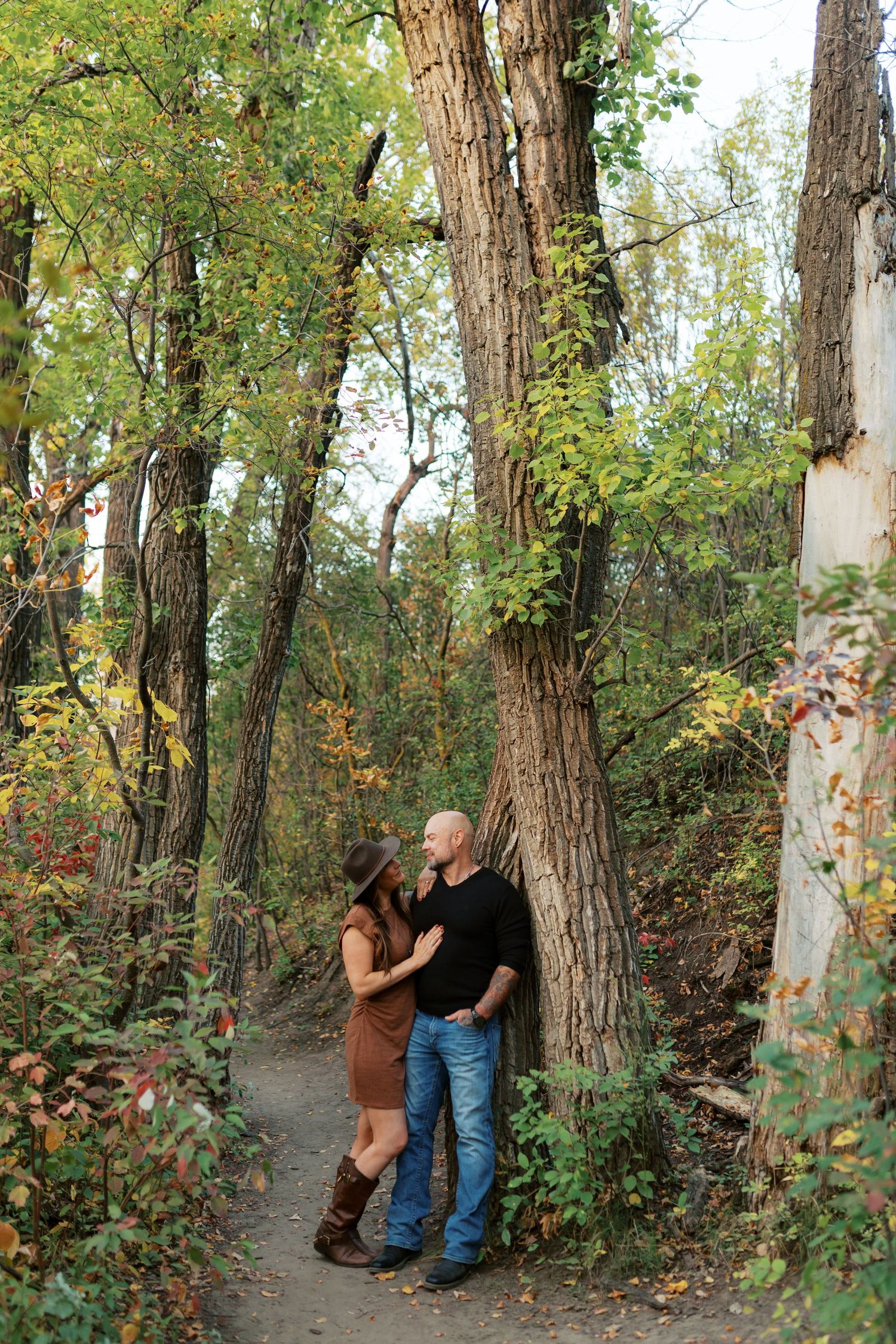 Couple sharing a romantic moment on a forest path surrounded by colorful autumn foliage and tall trees.