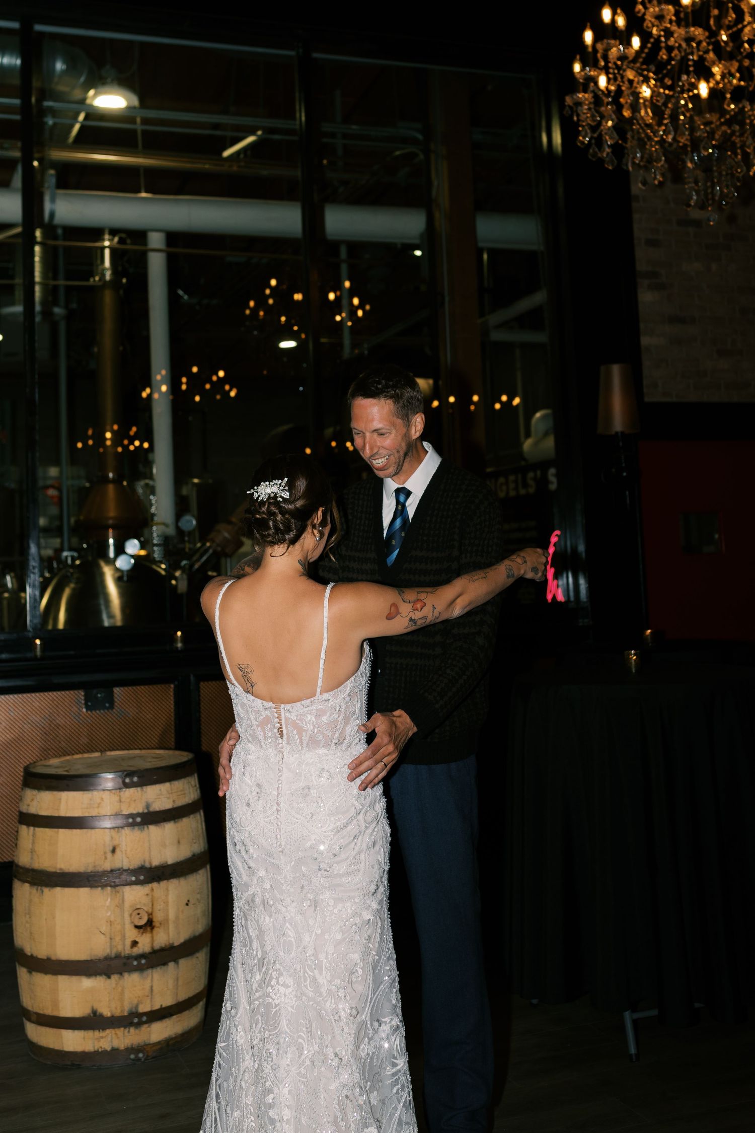 Bride and groom share their first dance in an elegant venue with warm chandelier lighting and rustic wine barrel decor.