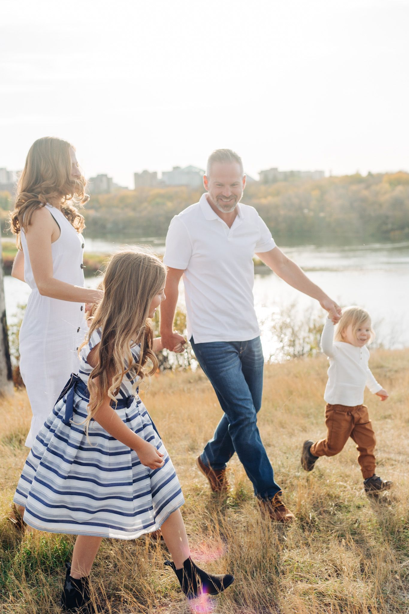 Family running and playing together in a golden field at sunset near a lake.
