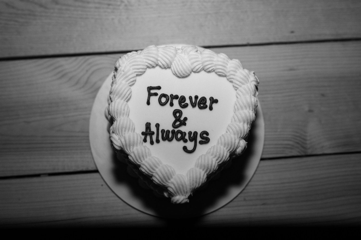 Black and white heart-shaped cake with Forever & Always written in dark frosting on a white plate.