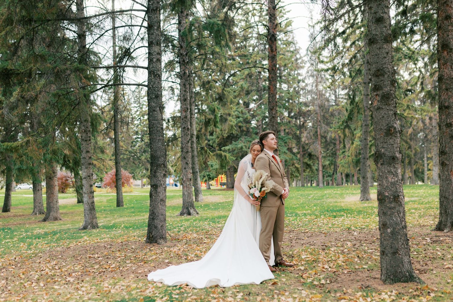 Wedding couple standing among tall pine trees in forest setting.