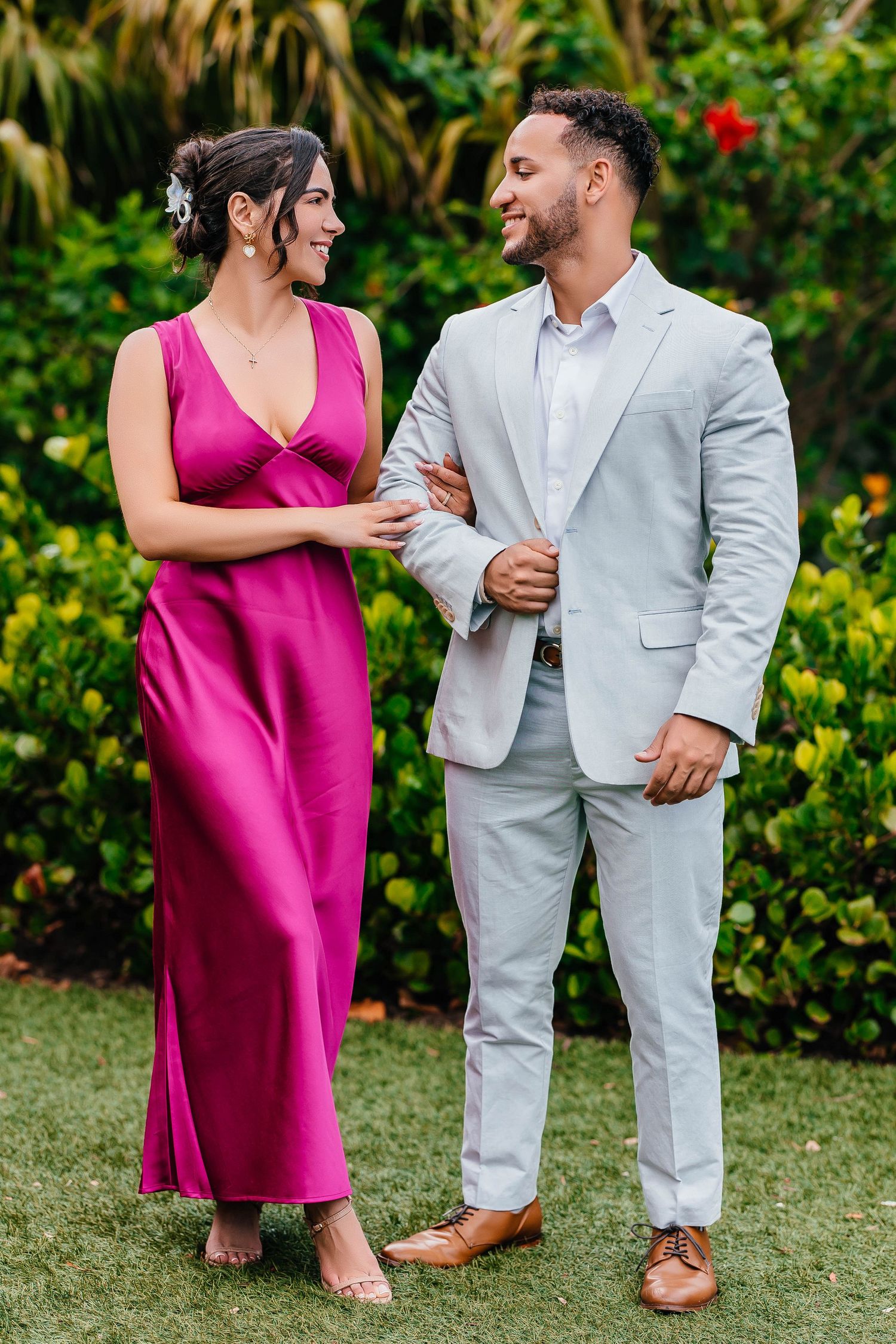 A couple in elegant attire shares a loving glance in a garden setting.