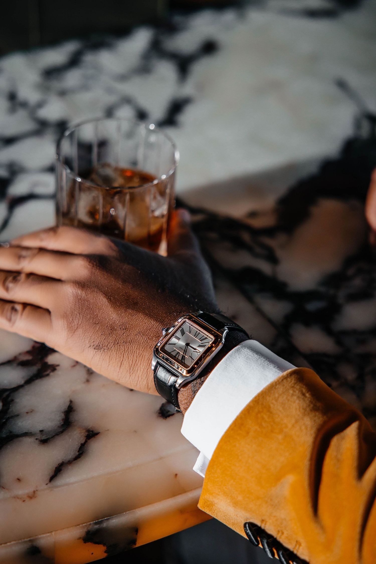 Close-up of hand wearing elegant watch holding drink on marble countertop.