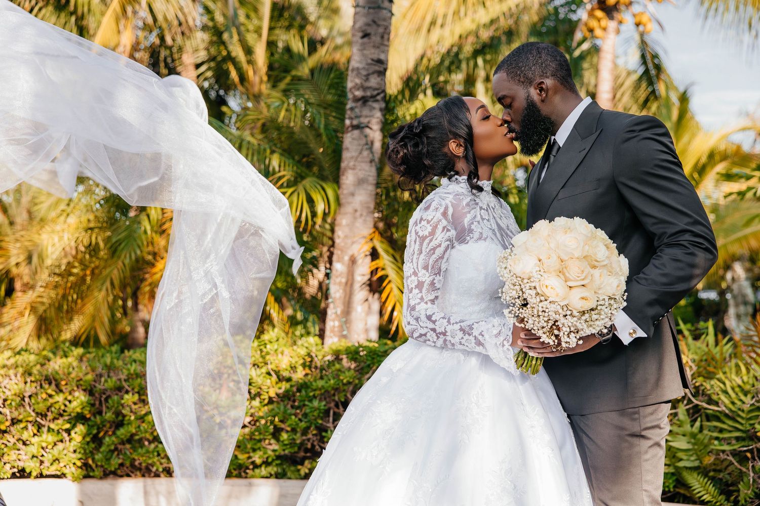 A romantic wedding kiss captured in a tropical garden setting with flowing veil.