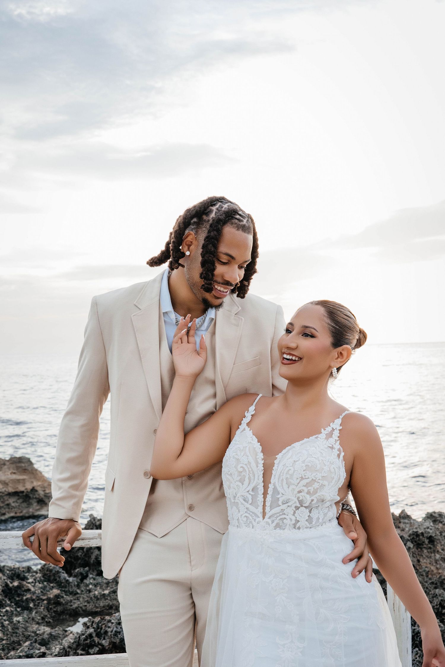 Joyful wedding couple sharing a candid moment while posing on coastal rocks by the ocean.