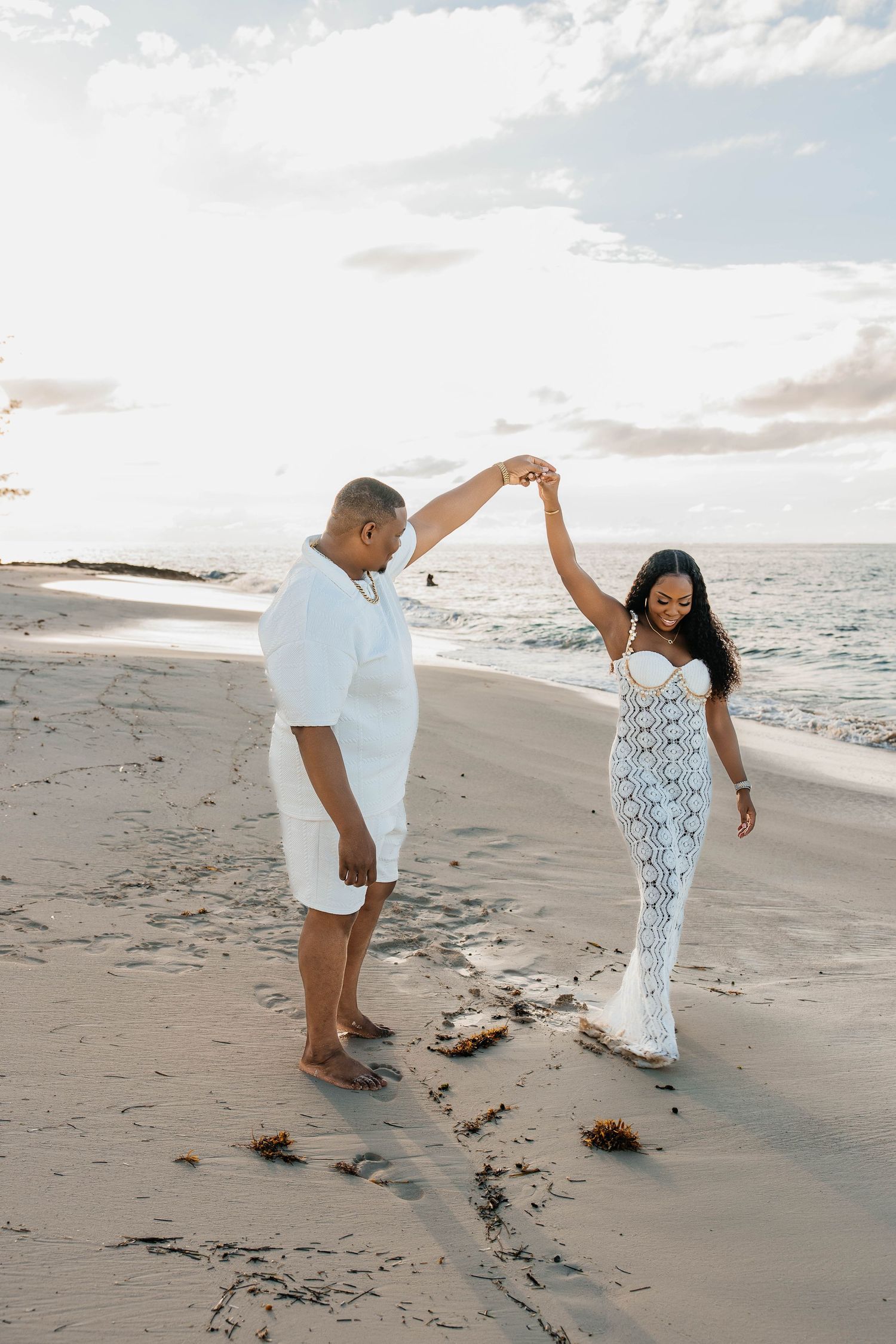 A couple dances together on a sandy beach at sunset, creating romantic silhouettes against the ocean backdrop.