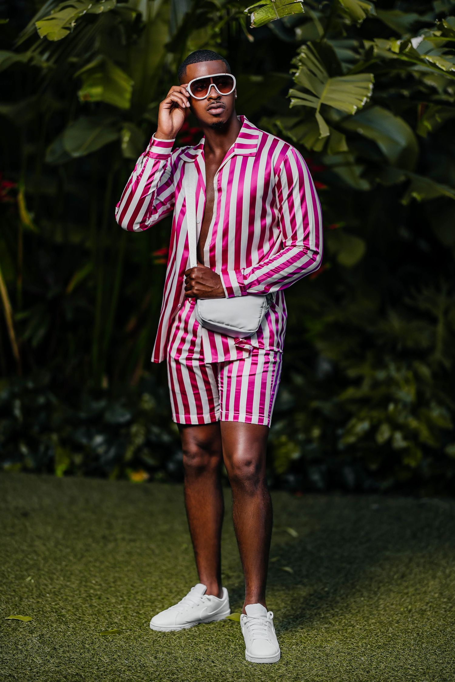 Pink and white striped shorts suit with sunglasses and white sneakers in garden setting.