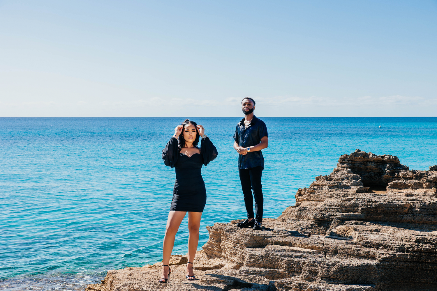 Happy couple enjoying a moment together on rocky cliffs overlooking bright blue ocean waters.
