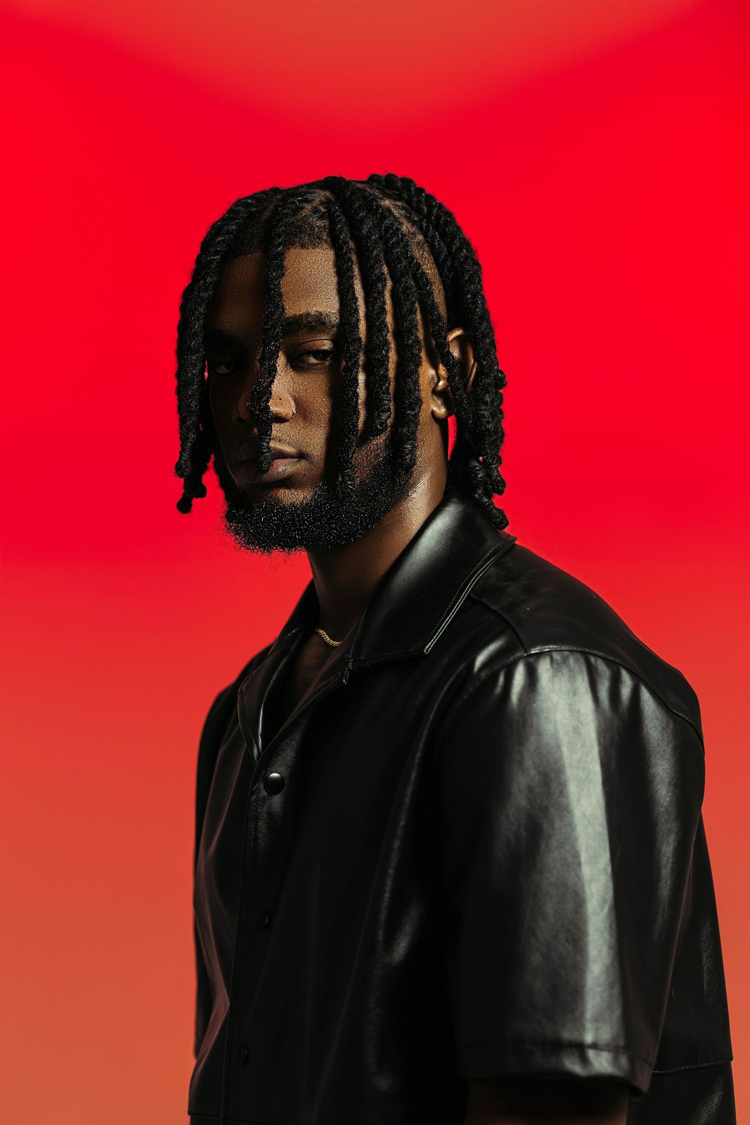 Artistic profile portrait against vibrant red background showing silhouette with dreadlocks in dark clothing.