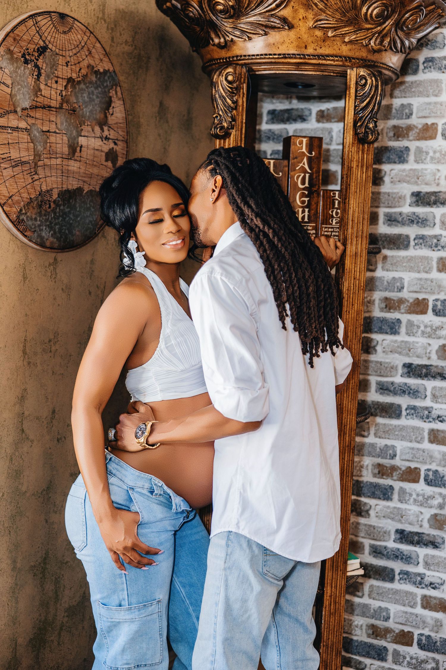 Intimate maternity photo with embracing couple against brick wall and vintage decor.