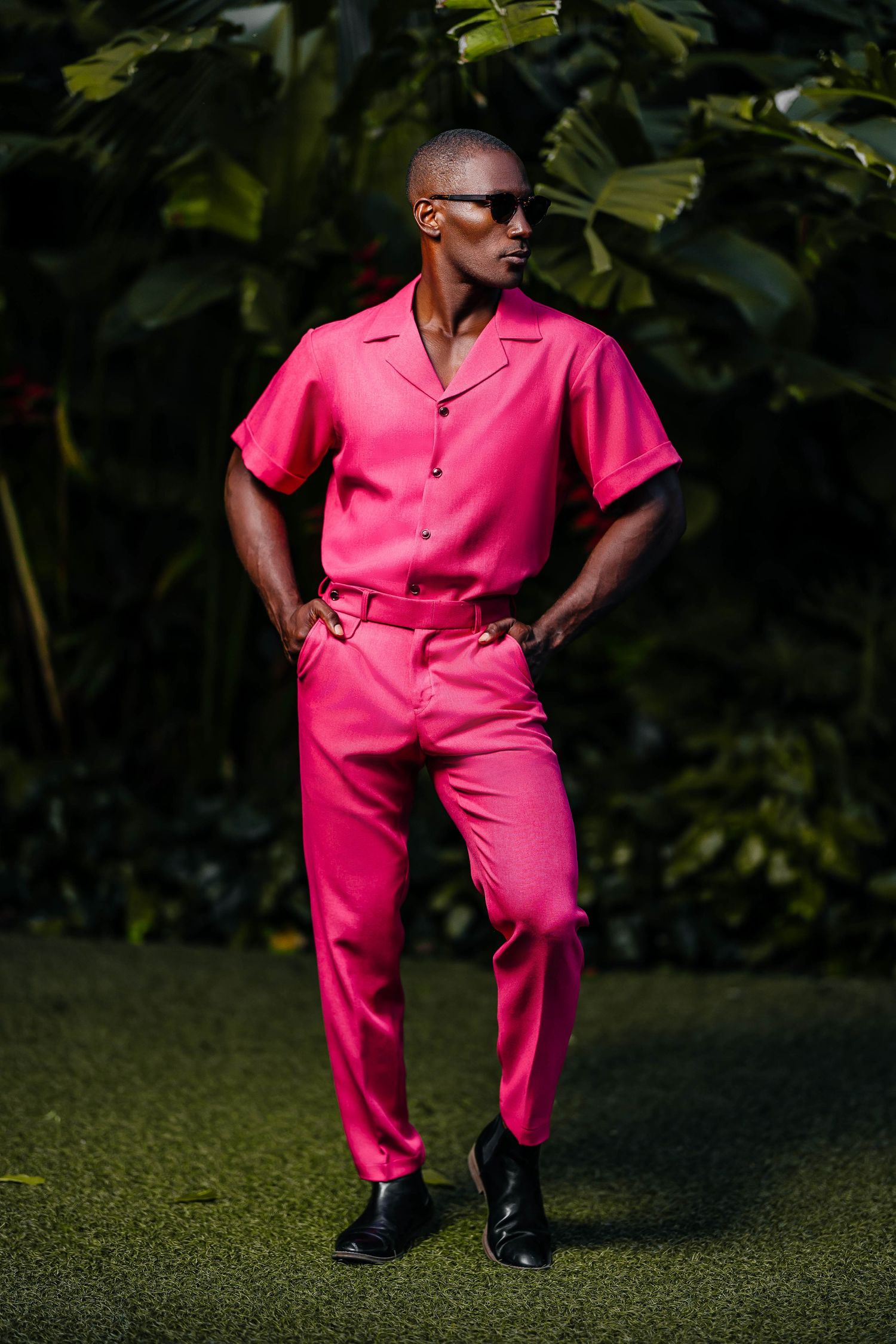 Vibrant pink short-sleeve shirt and matching pants ensemble in tropical garden setting.