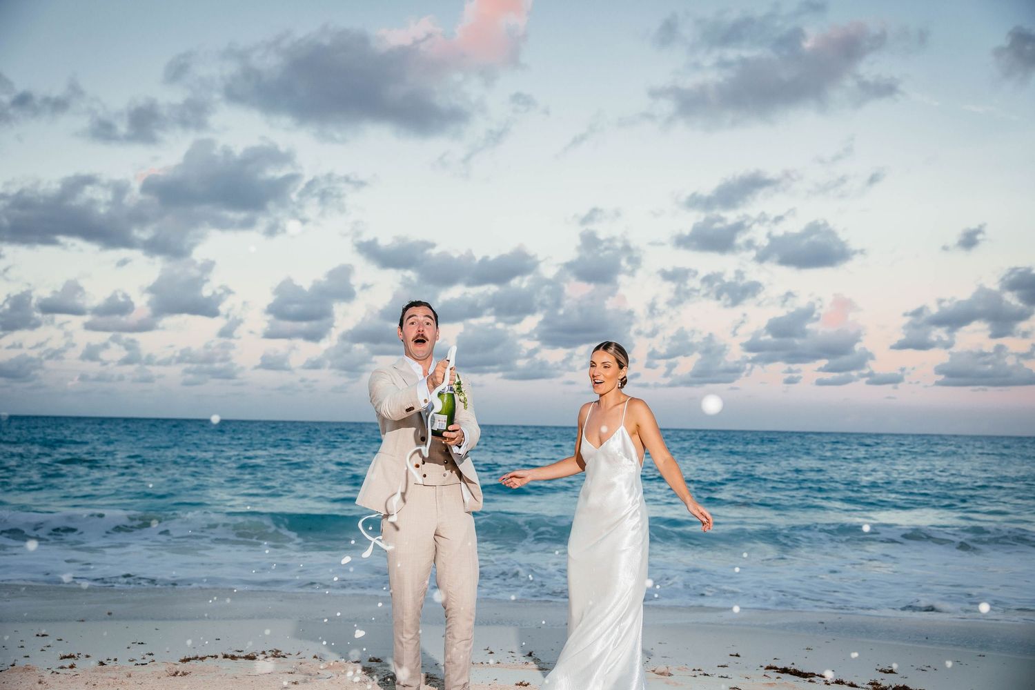 Newlyweds walking and laughing on beach at sunset with ocean waves.