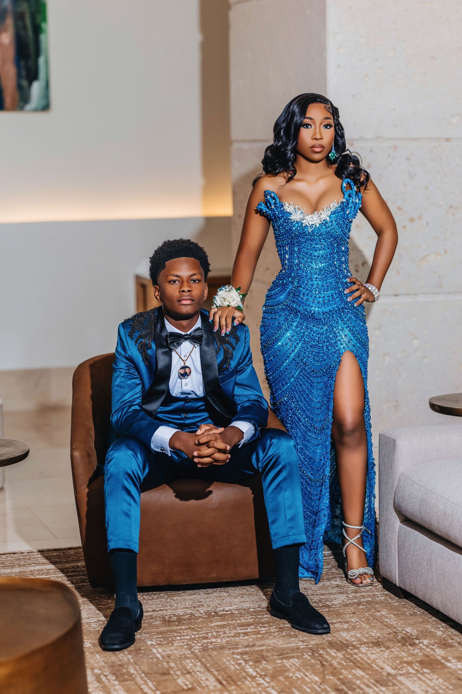 Glamorous couple in matching blue outfits pose together in an elegant living room setting for a formal event.