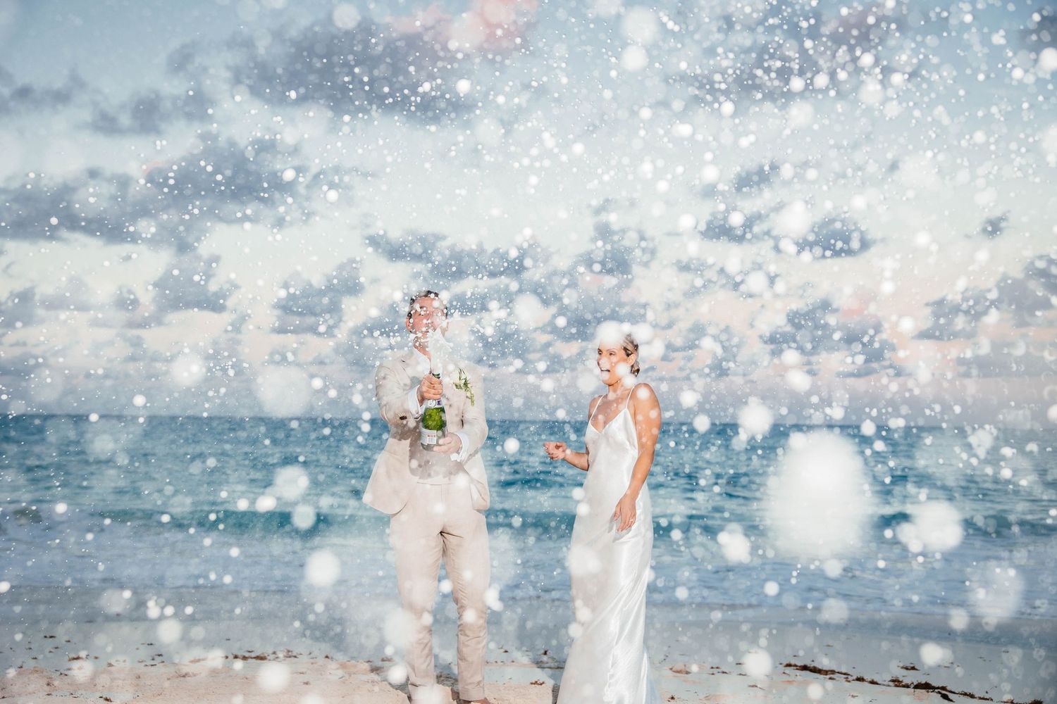 Beach wedding photo with water splashing around couple in elegant attire.