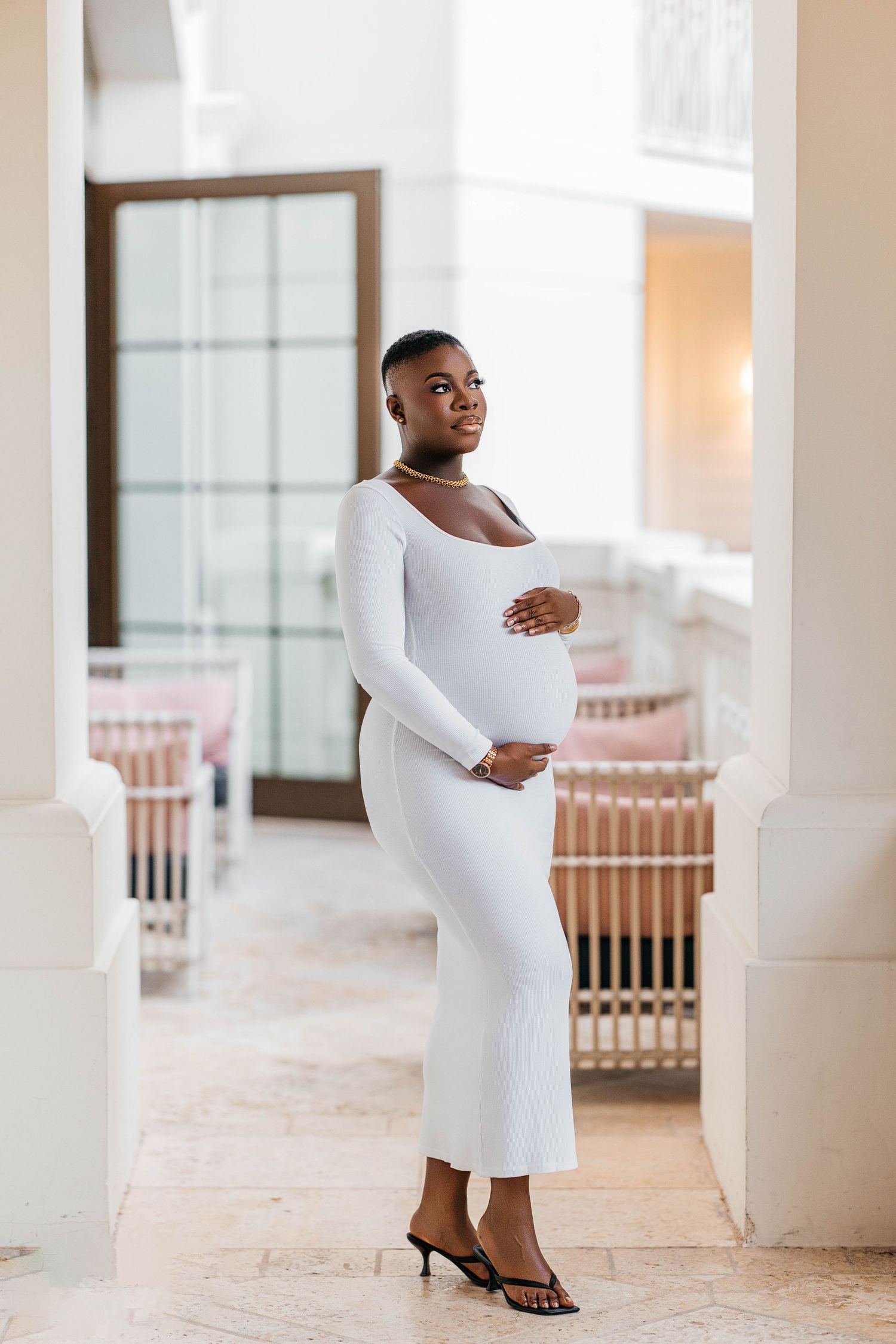 Elegant maternity fashion shot featuring a floor-length white dress and heels.