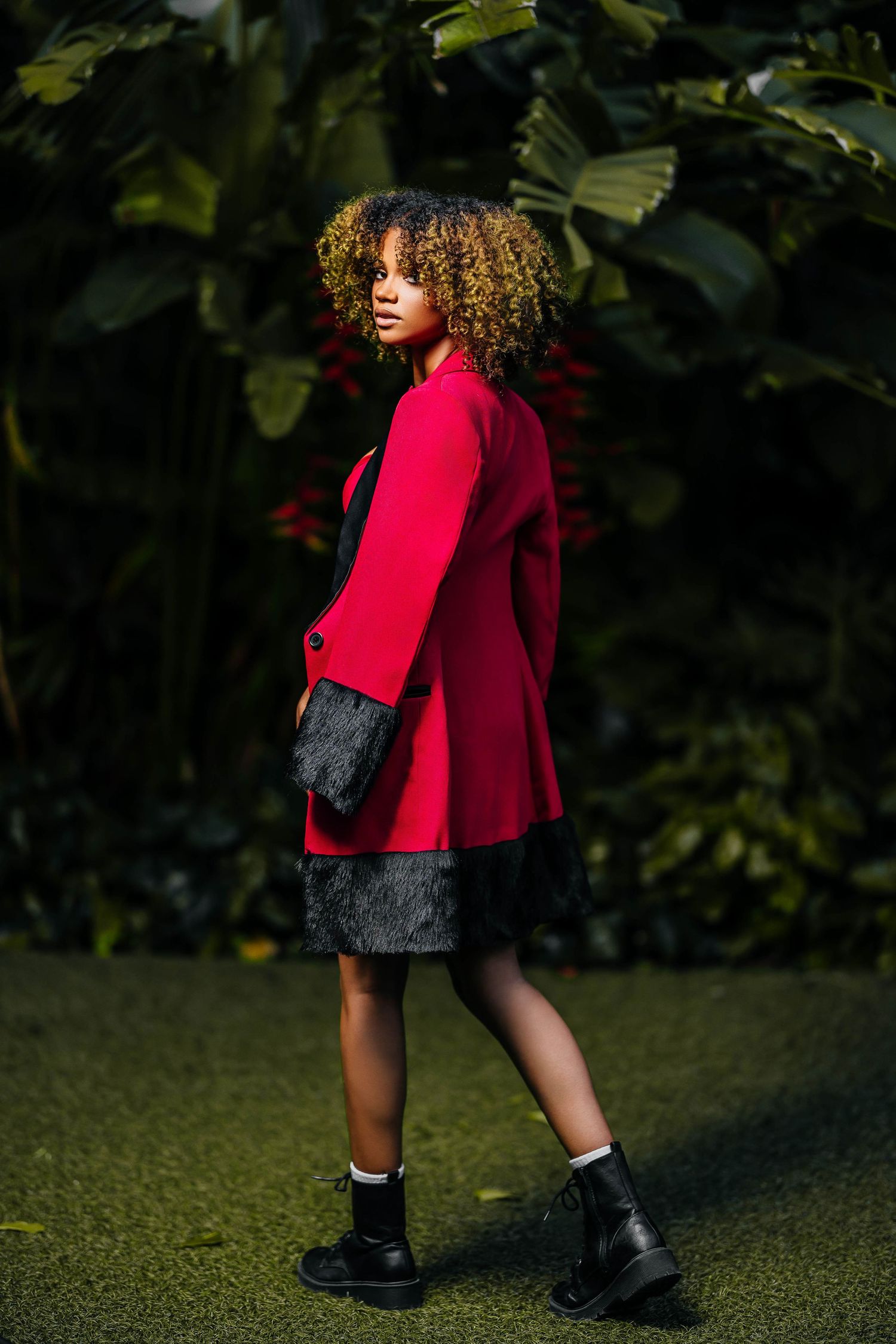 Red wool coat paired with black dress and combat boots against tropical foliage.