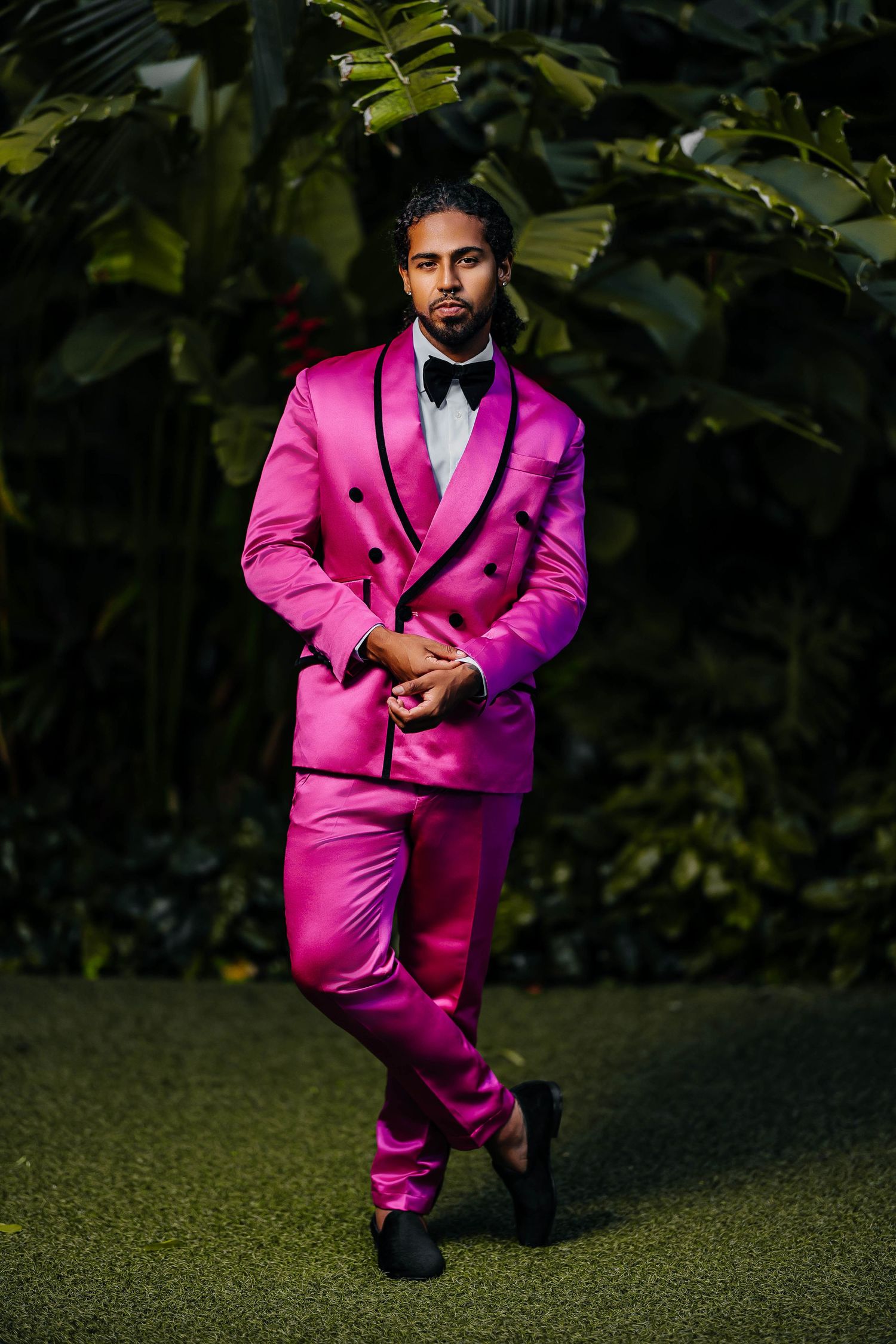 Hot pink double-breasted suit with black bow tie photographed against green foliage.