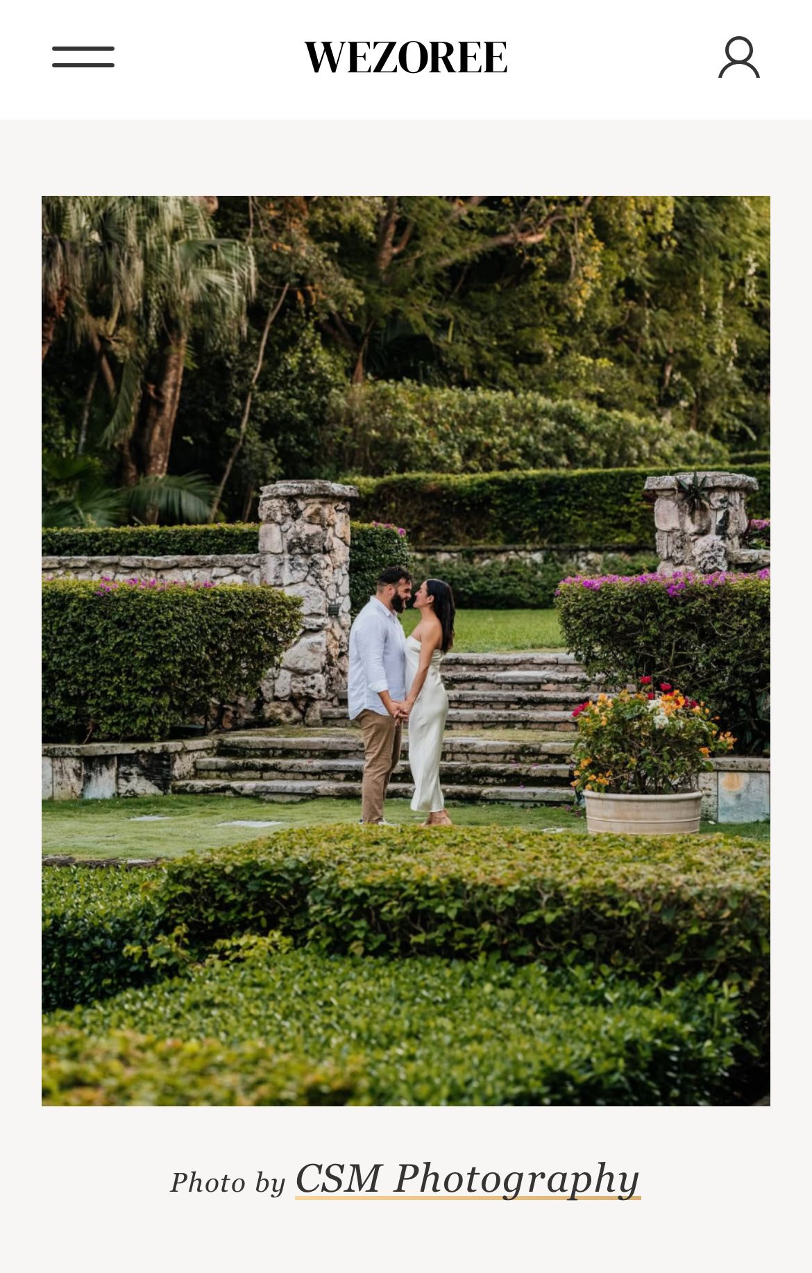 A romantic couple embraces on stone garden steps surrounded by lush greenery and flowers in an outdoor setting.