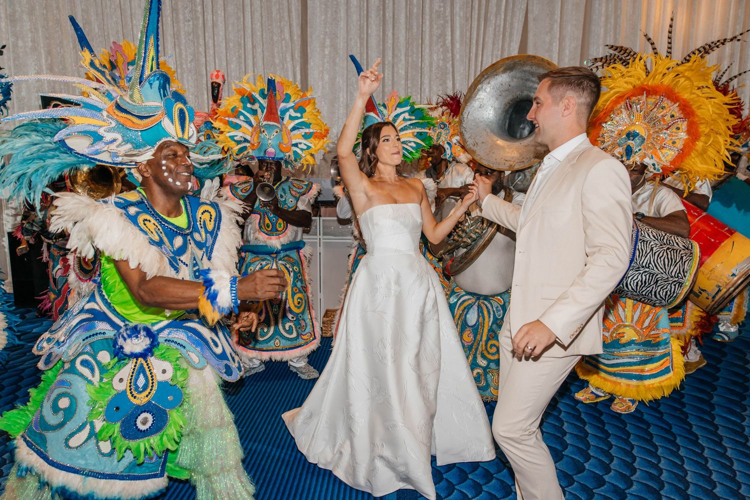 Bride and groom dancing with colorful Junkanoo performers in vibrant costumes at a wedding reception.