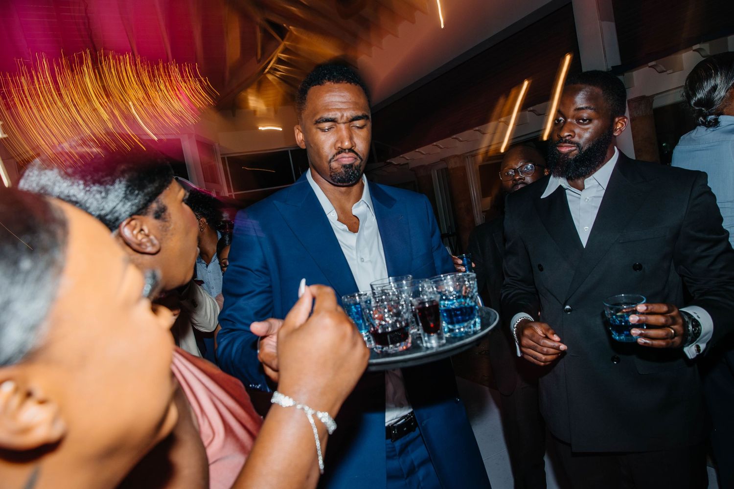 Man in blue suit serving drinks on a tray at an elegant evening social event or party.