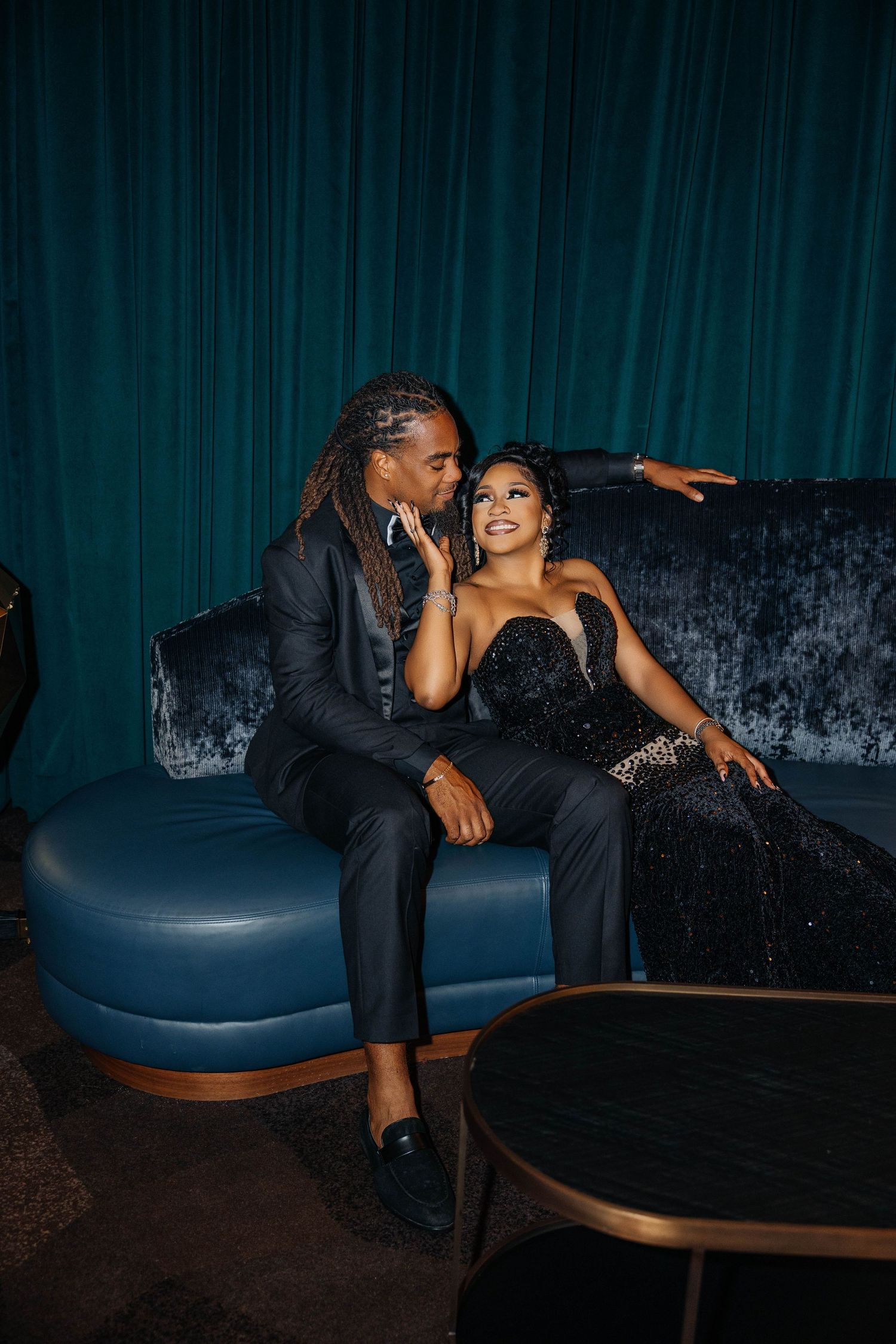Couple in formal attire sharing an intimate moment on a blue velvet couch.