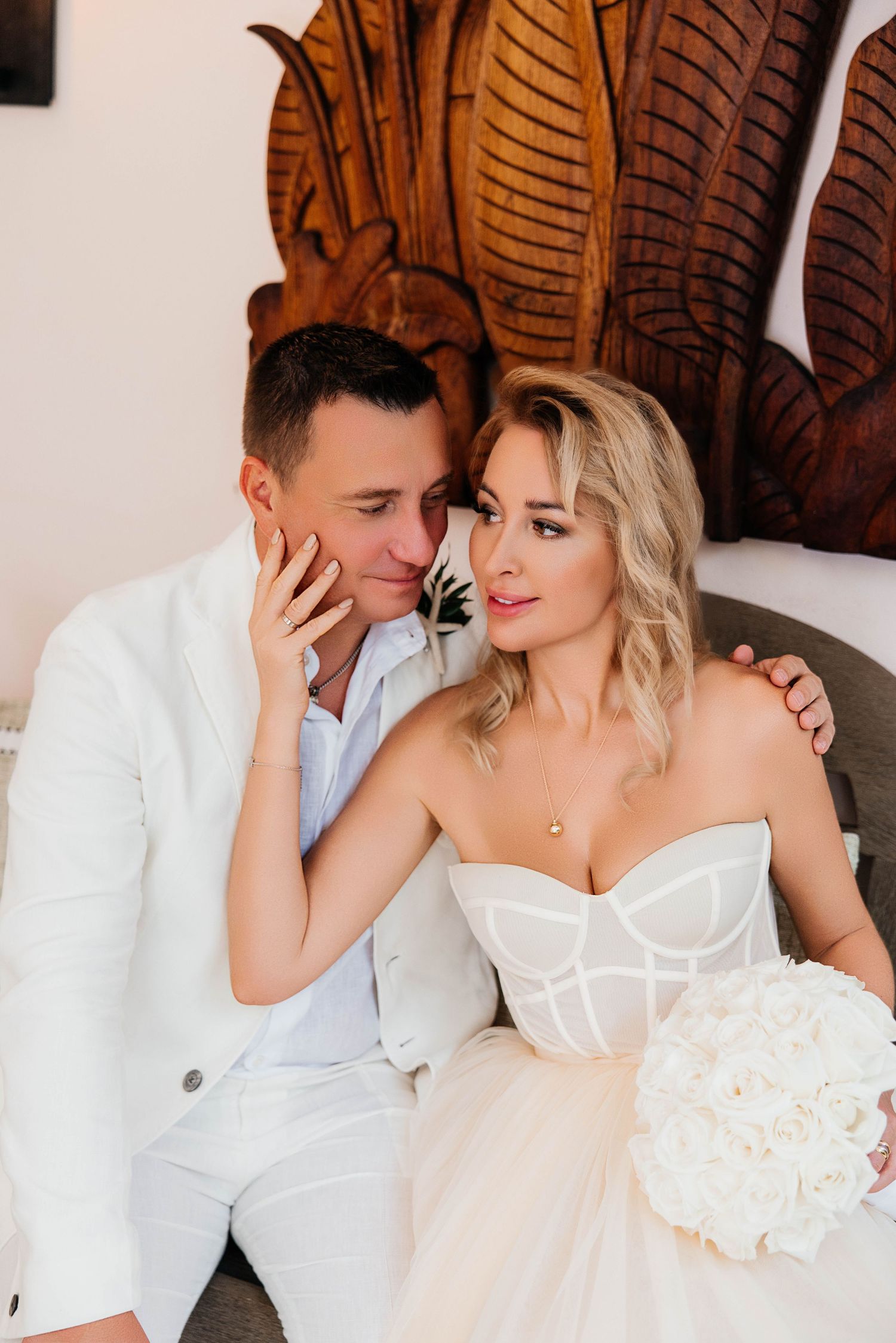 An intimate wedding portrait with a carved wooden wall backdrop and white florals.
