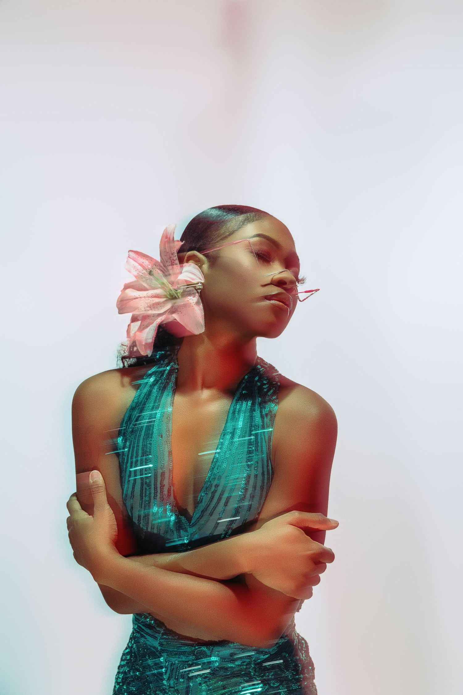 Fashion portrait of a model in turquoise dress with pink flower accessory against white background.