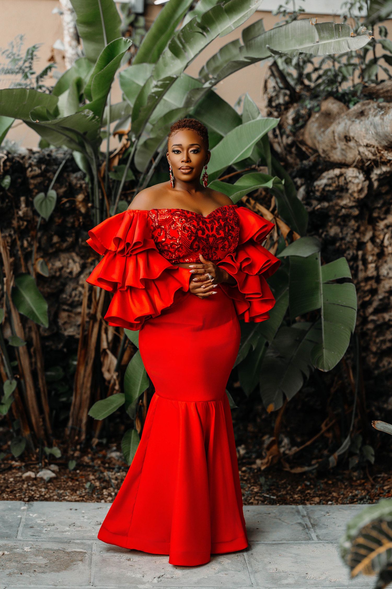 Dramatic red mermaid gown with tiered ruffles photographed in tropical garden setting.