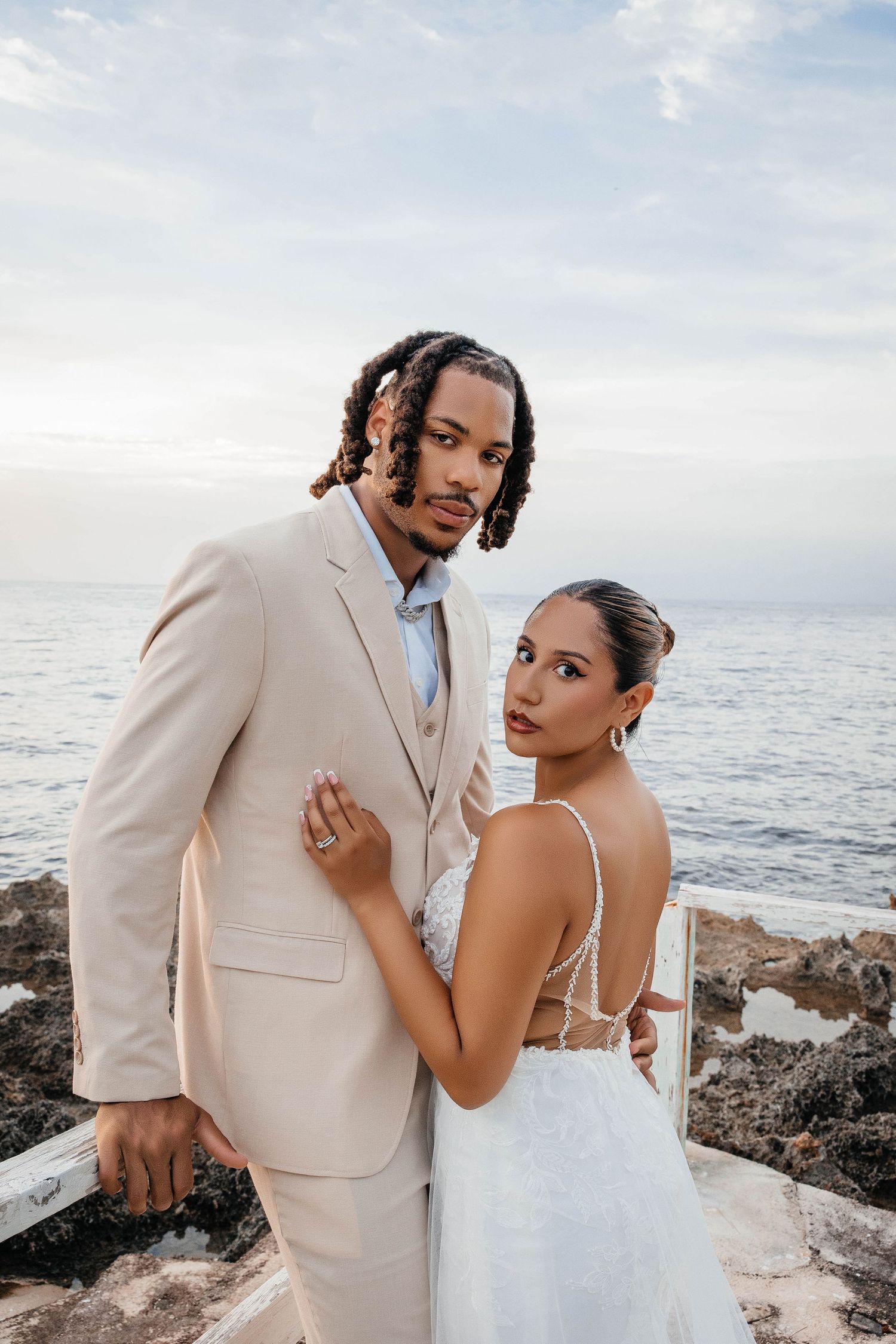 Stylish wedding portrait of couple in cream and white attire against ocean background.