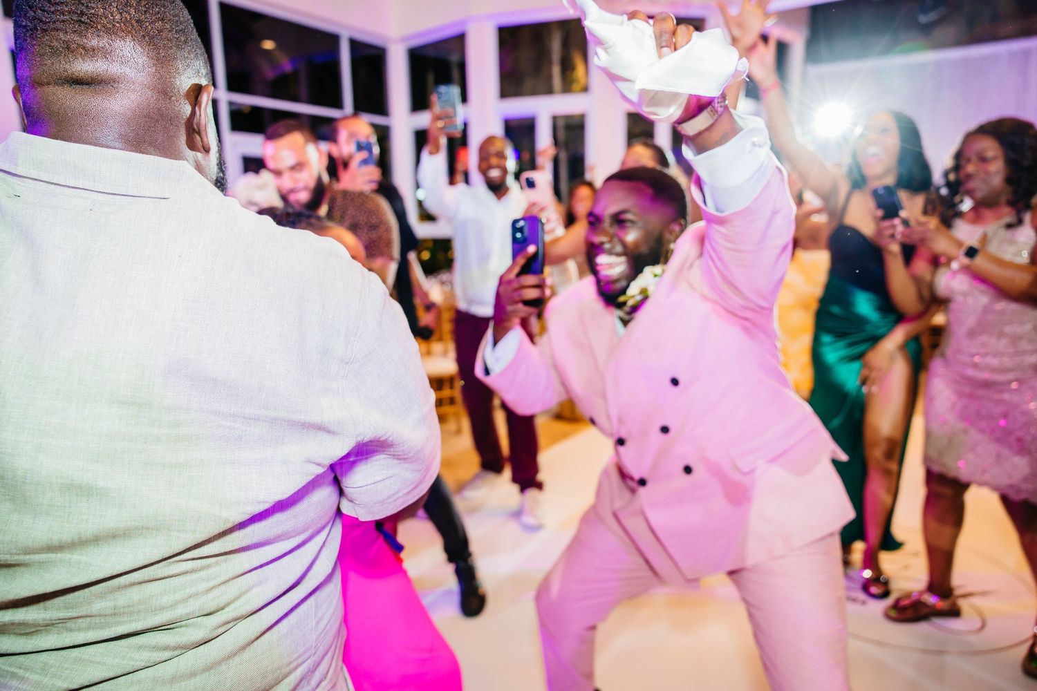 Man in pink suit dancing energetically at a lively wedding reception party.