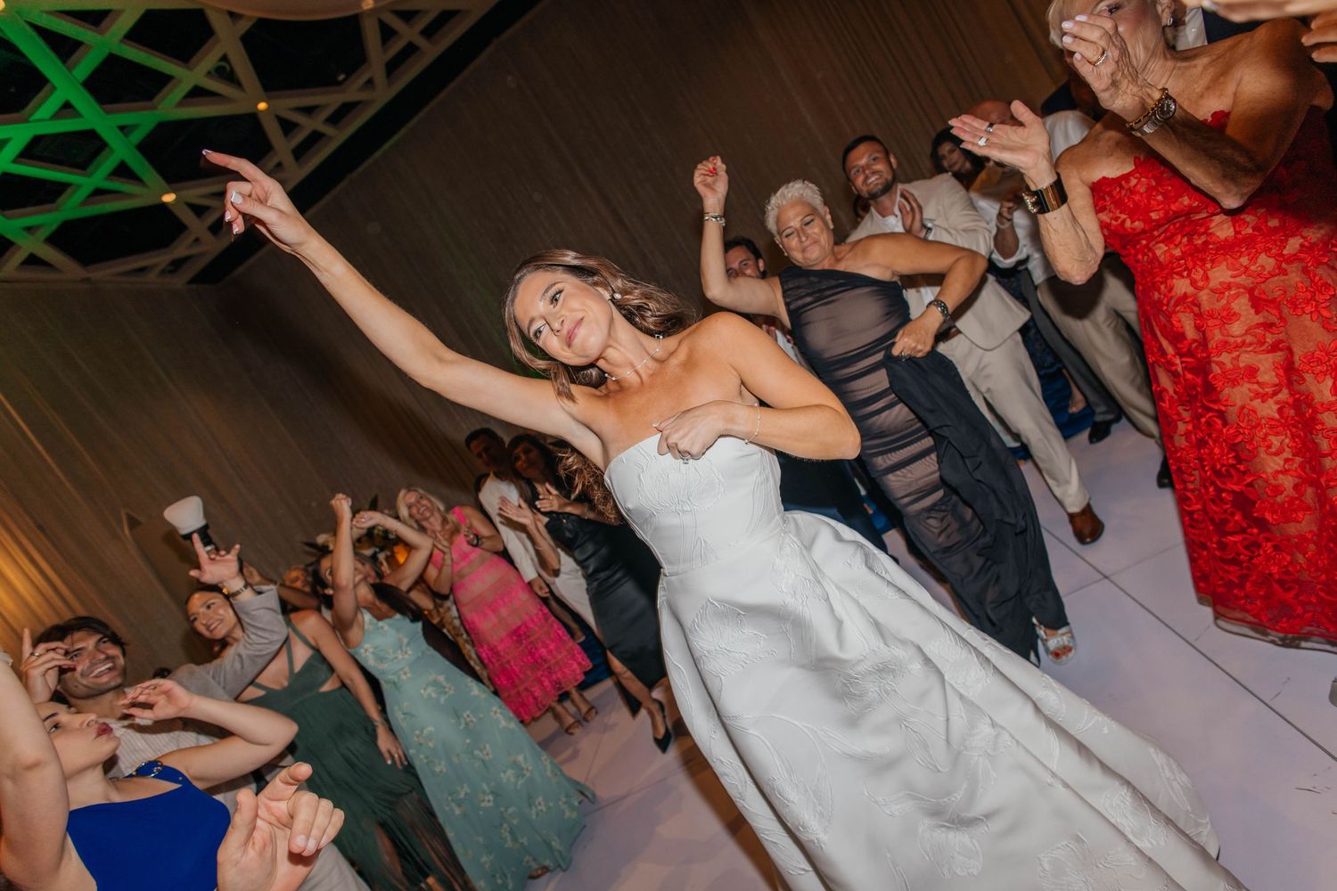 Bride in white gown dancing joyfully with guests at a lively wedding reception party.