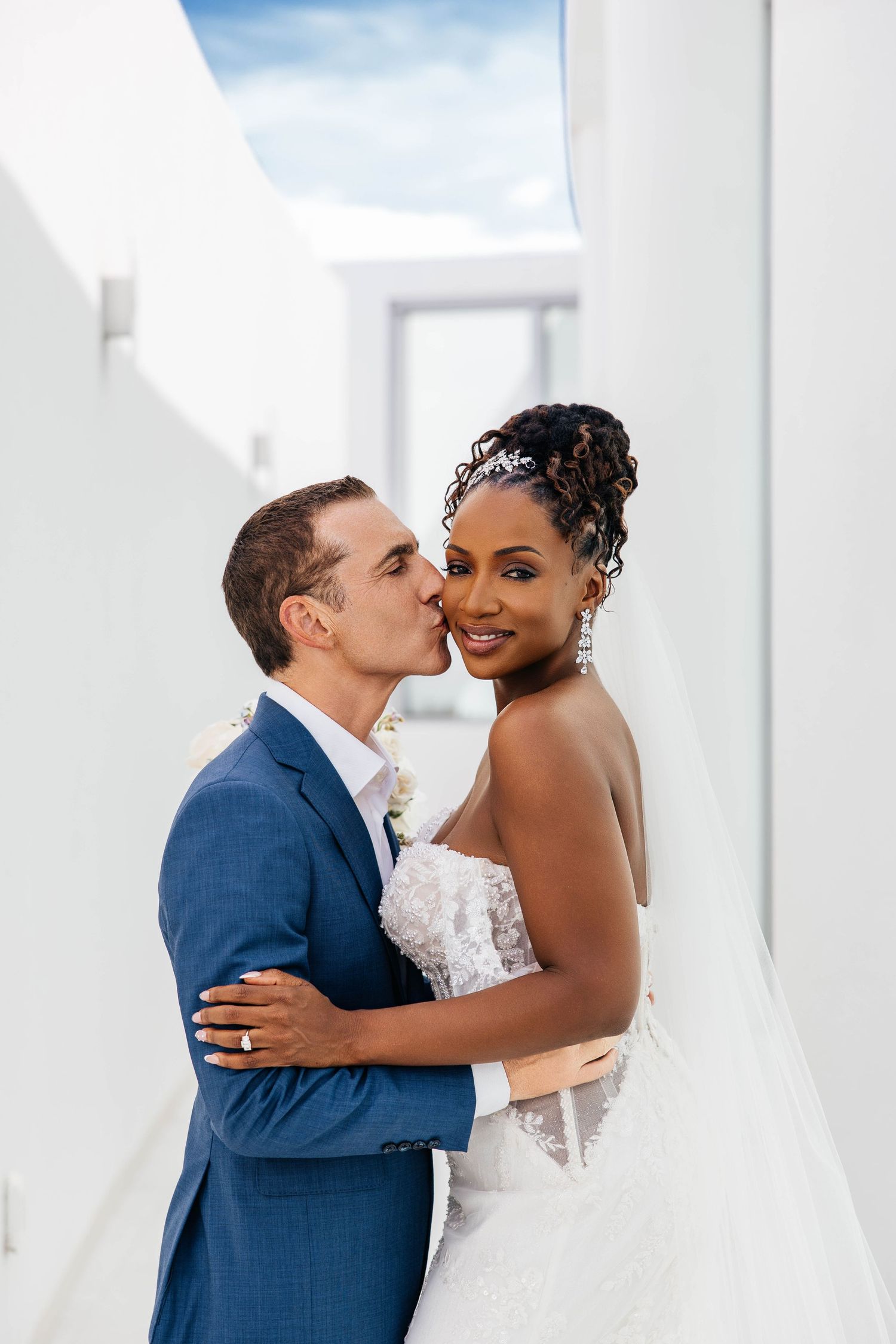 Happy couple sharing romantic kisses while wearing formal wedding attire in bright white modern setting.